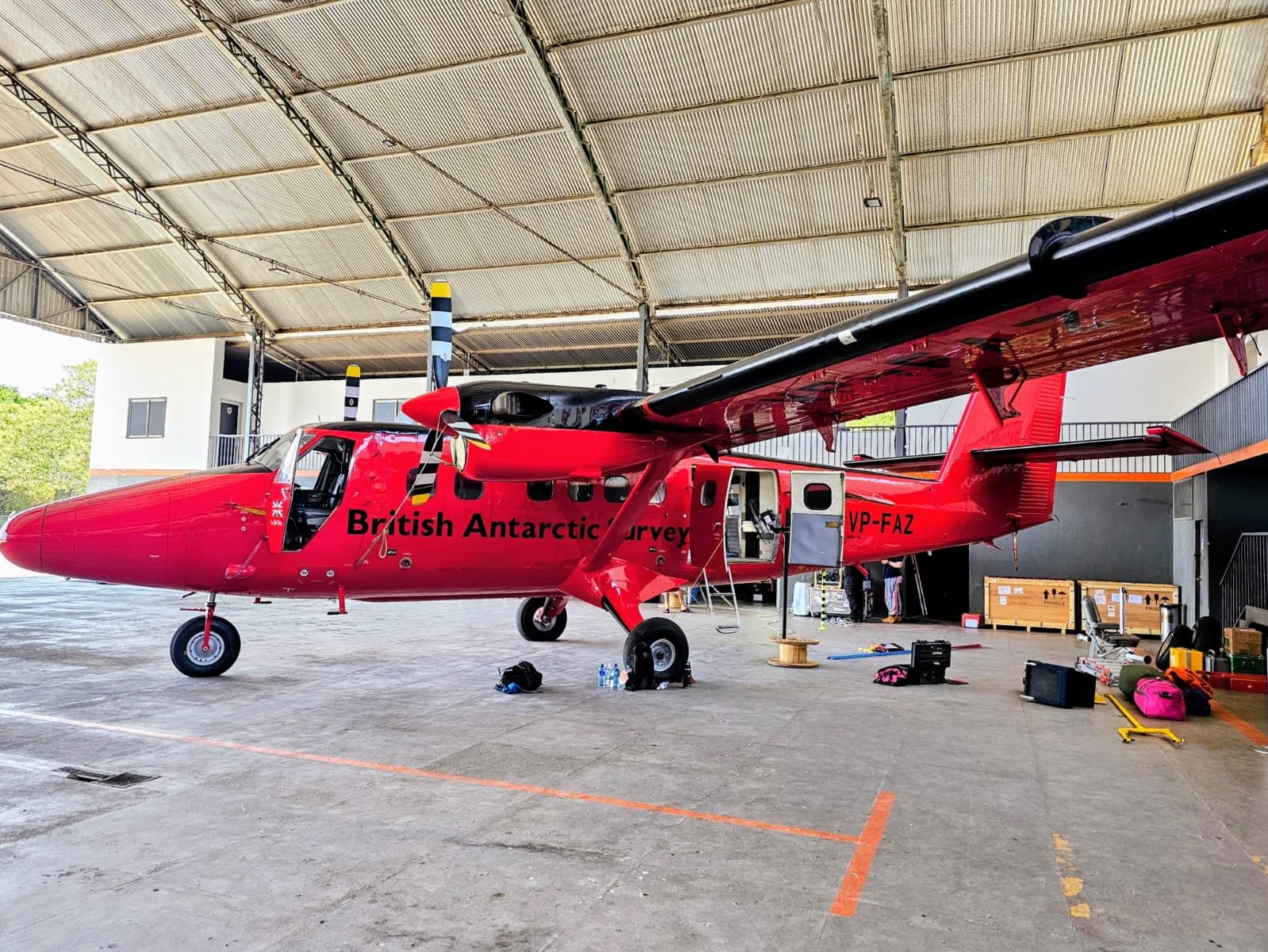 Avião de pesquisa vermelho dentro de um hangar, com caixas de equipamentos ao redor