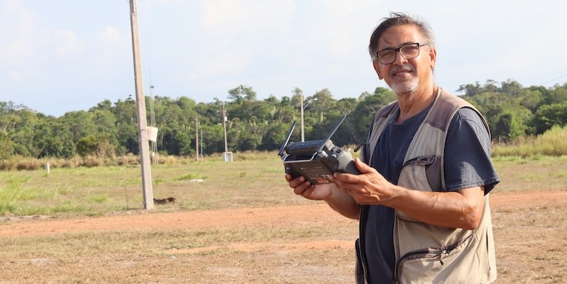 Pesquisador segura o controle de um drone em uma área aberta, com a floresta ao fundo