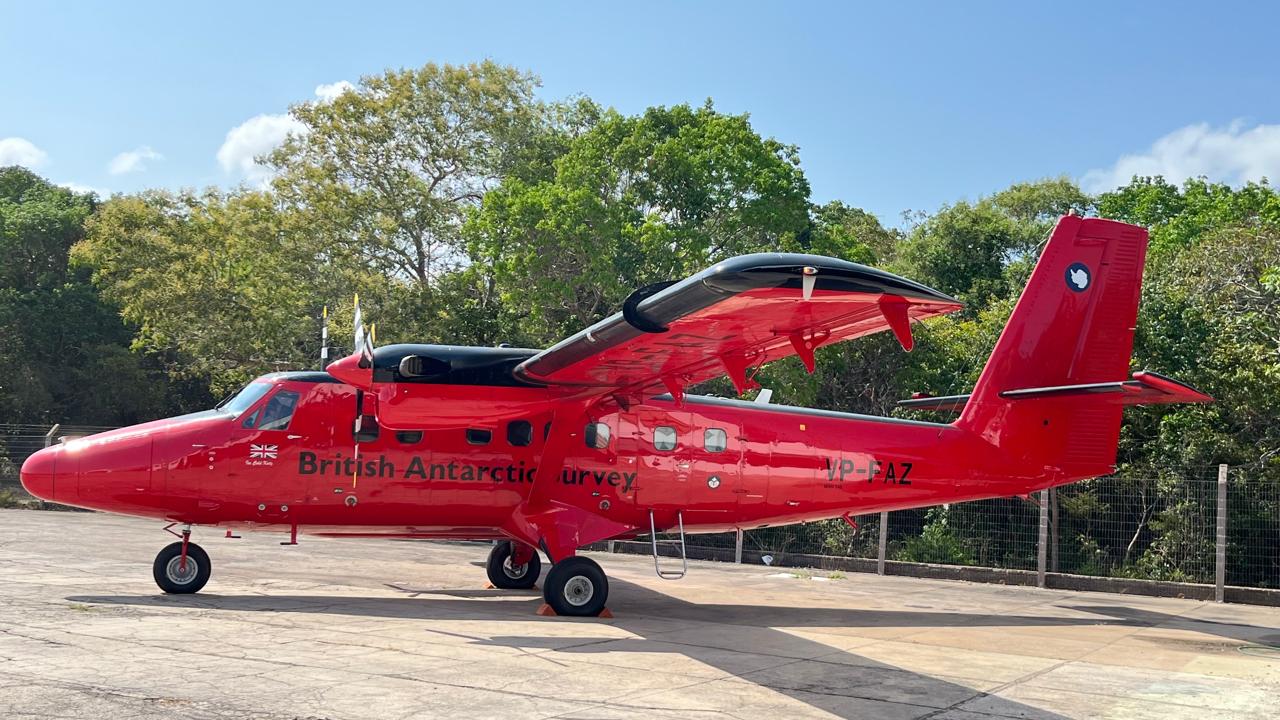 Avião bimotor vermelho estacionado no pátio, com árvores ao fundo